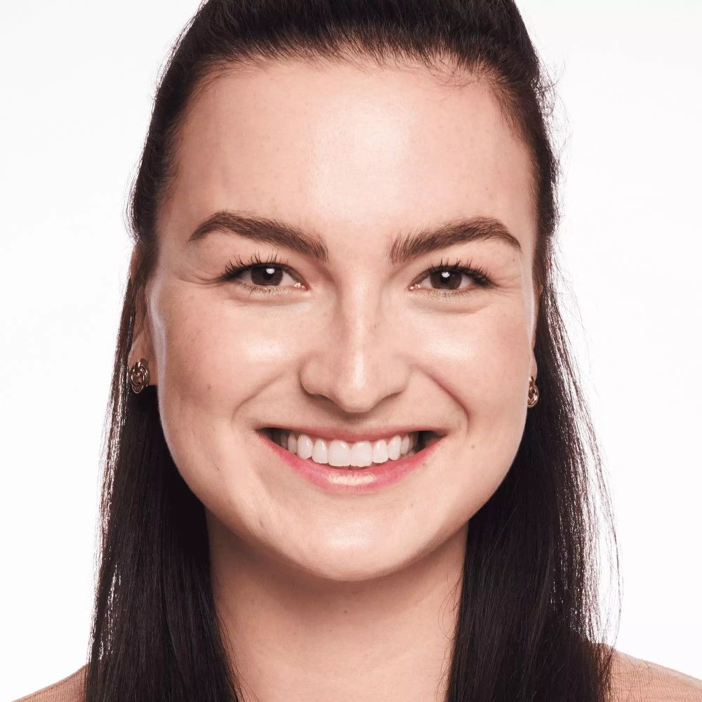 Gros plan sur le visage souriant d'une femme. La peau semble uniforme et éclatante.