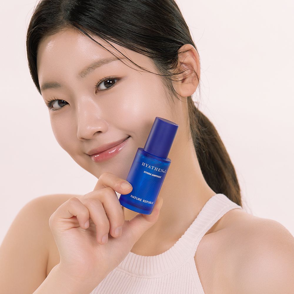 Femme tenant un flacon de sérum bleu. Inscription: HYATHENOL Hydra Ampoule, NATURE REPUBLIC. La femme sourit.