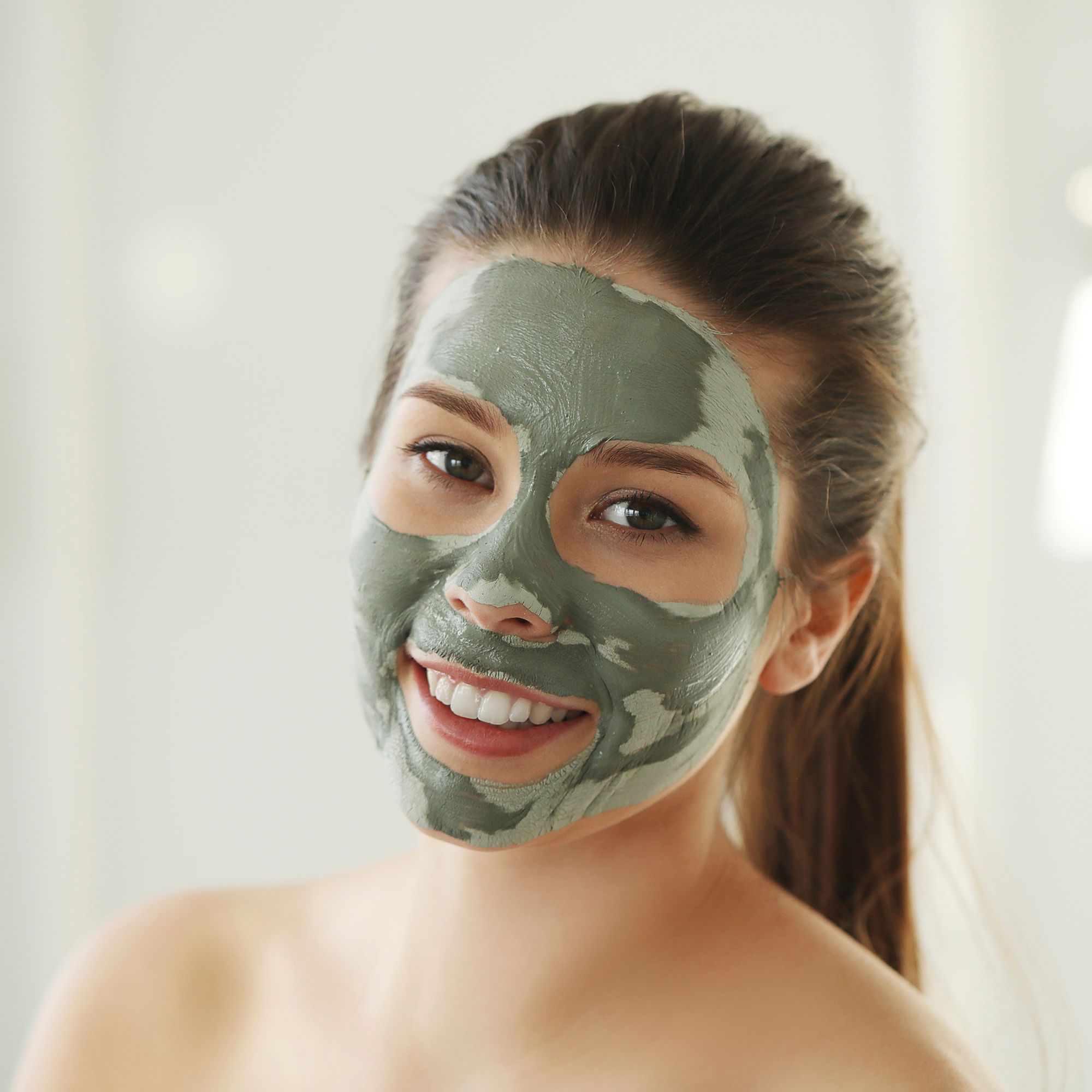 Vrouw met groen kleimasker op haar gezicht. Ze lacht.