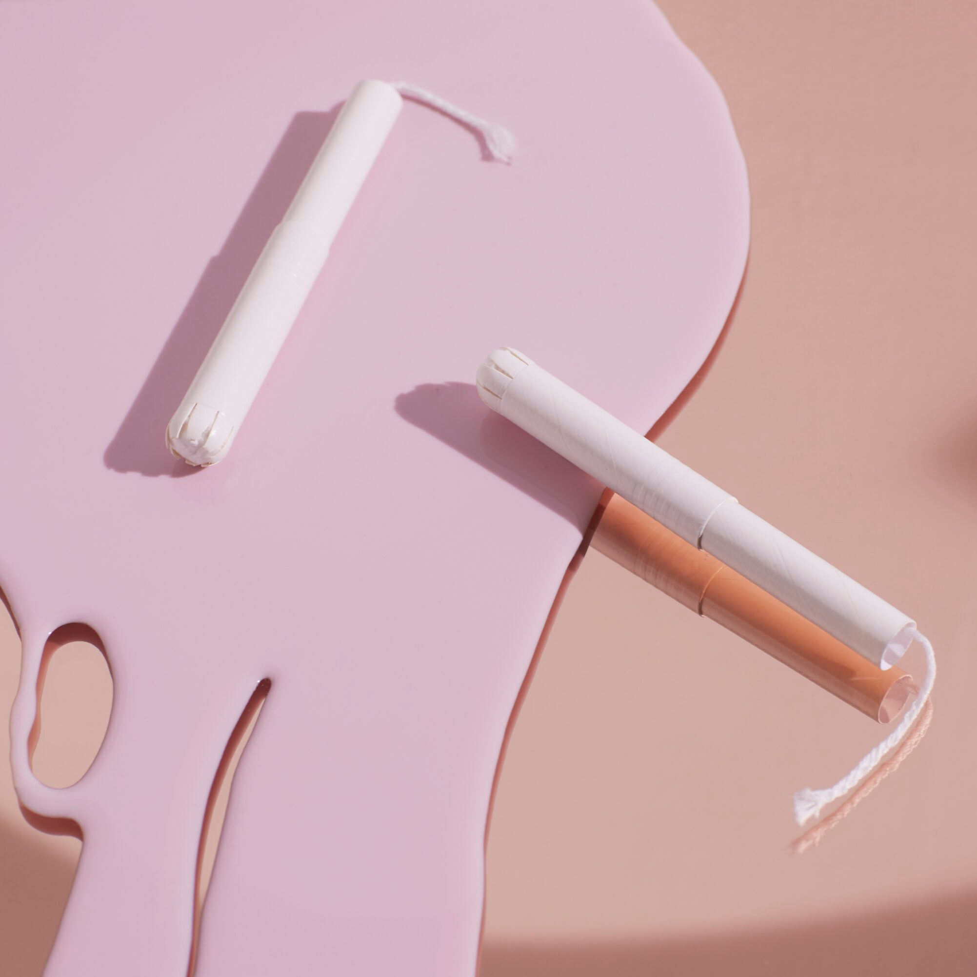 Deux tampons blancs avec applicateur sur surface rose. Un tampon avec fil.