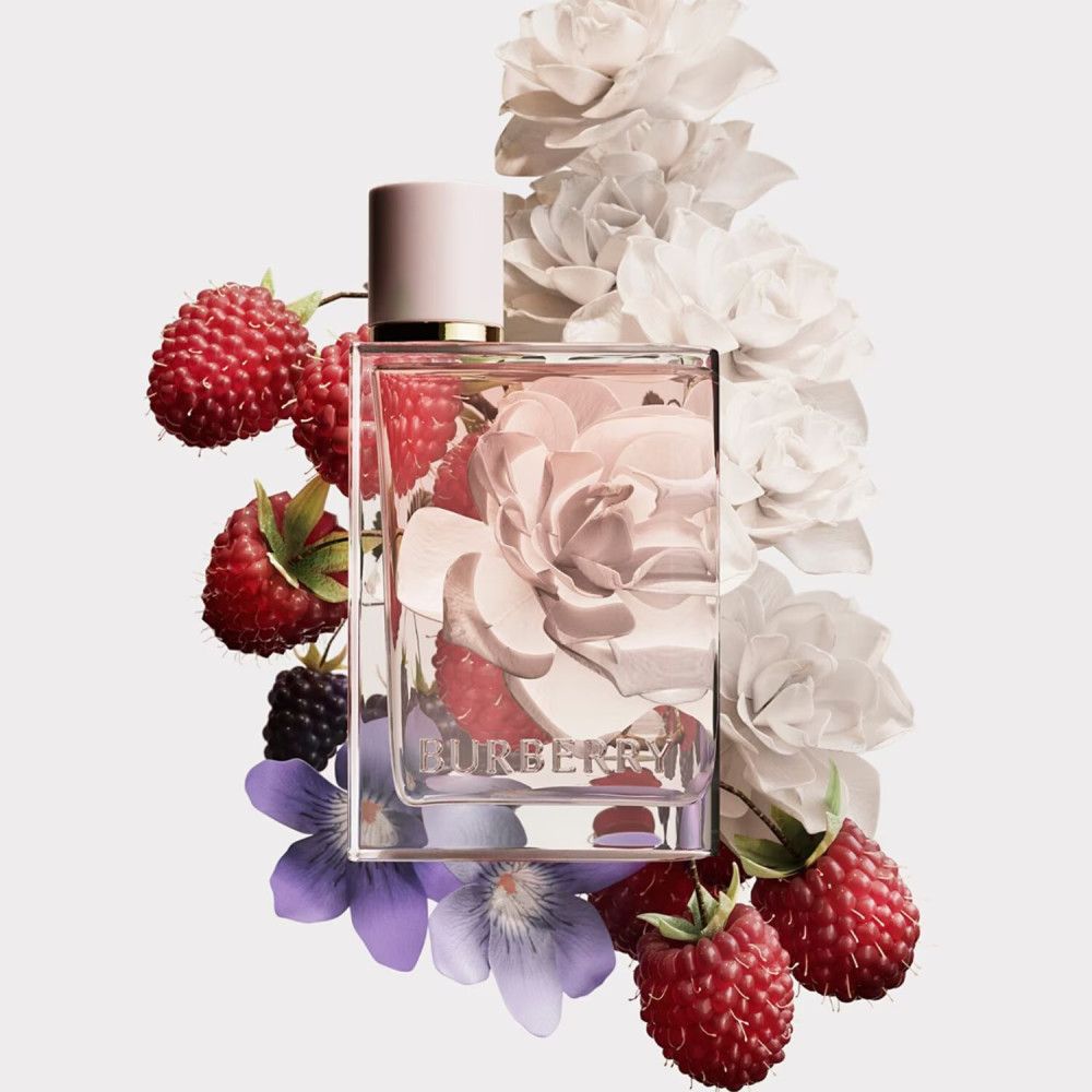 Flacon Burberry Her Eau de Parfum, entouré de framboises, mûres, fleurs et pétales. Le flacon est de forme carrée.
