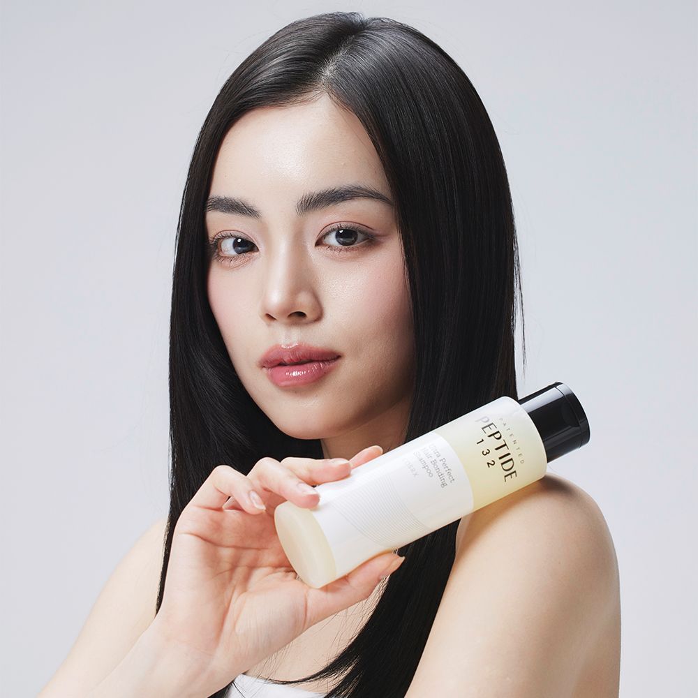 Femme aux longs cheveux noirs tenant une bouteille de shampoing PEPTIDE-132.