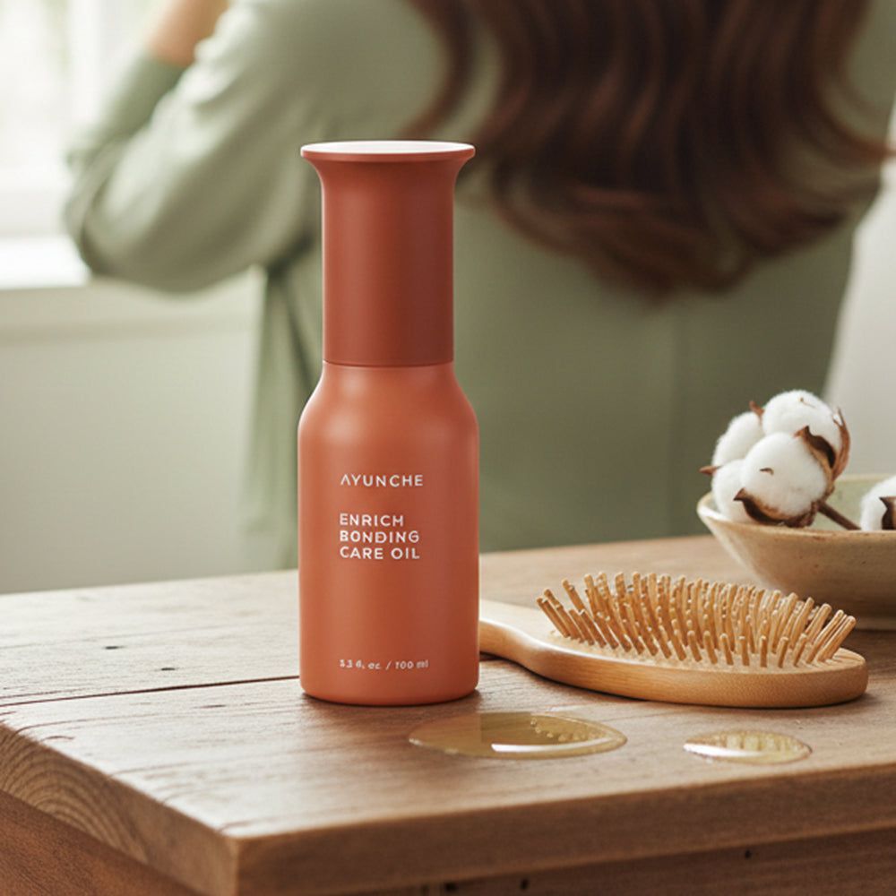 Fles AYUNCHE Enrich Bonding Care Oil naast haarborstel en wattenbolletjes op houten tafel.