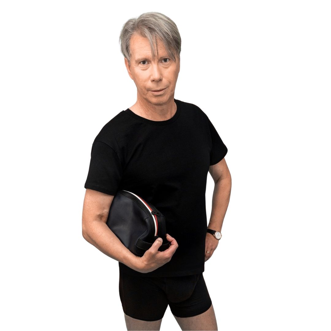 Homme aux cheveux gris tenant une trousse noire. Porte un t-shirt noir et un boxer.