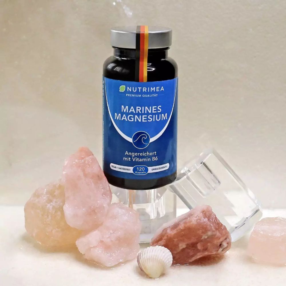 Fles MAGNESIUM met vitamine B6, omringd door roze stenen en een schelp. Met Duitse vlag.