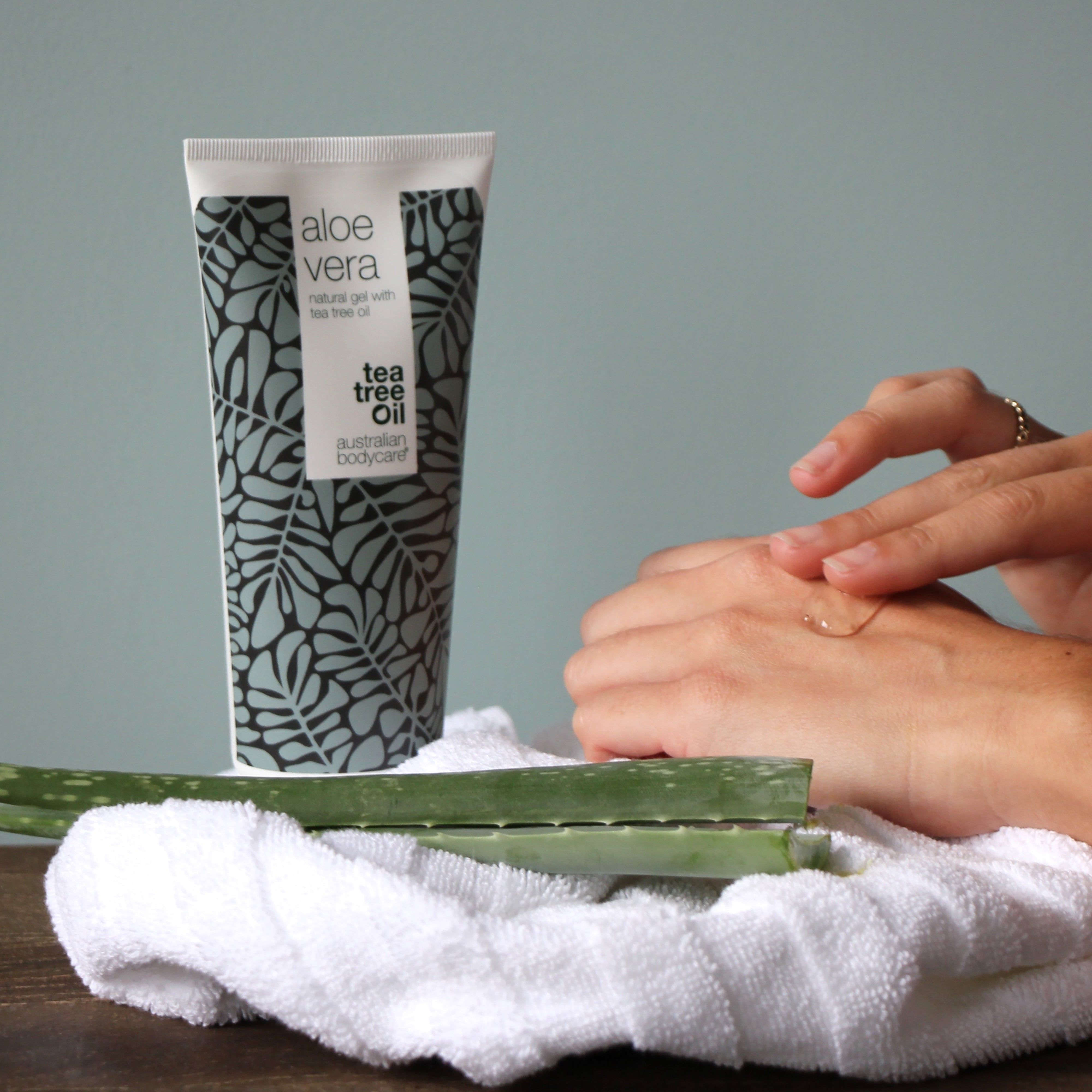 Personne applique du gel sur sa main. Tube de gel d'aloe vera, motif de feuilles grises. Inscription : Aloe Vera, Tea Tree Oil, Australian Bodycare.
