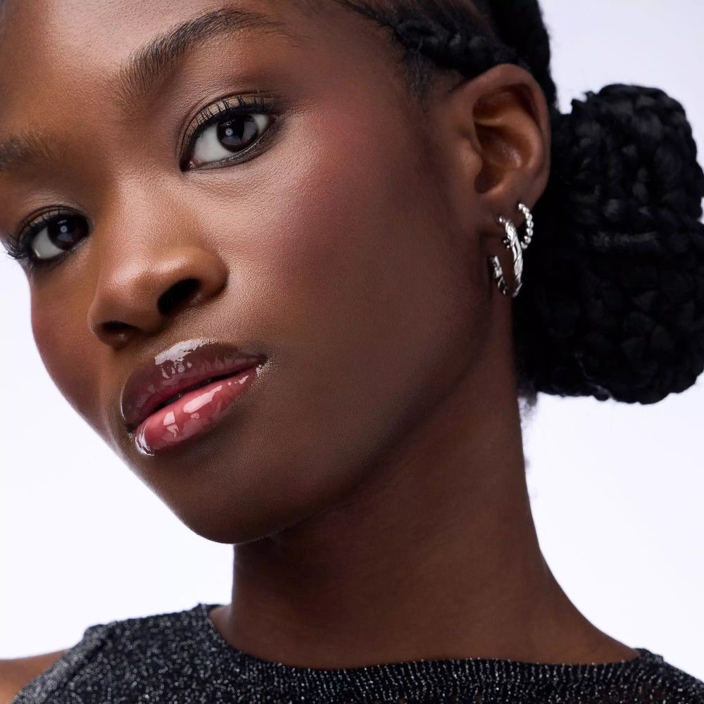 Portret van een vrouw met glanzende lipolie. Glanzende lippen, donkere huid, knot.