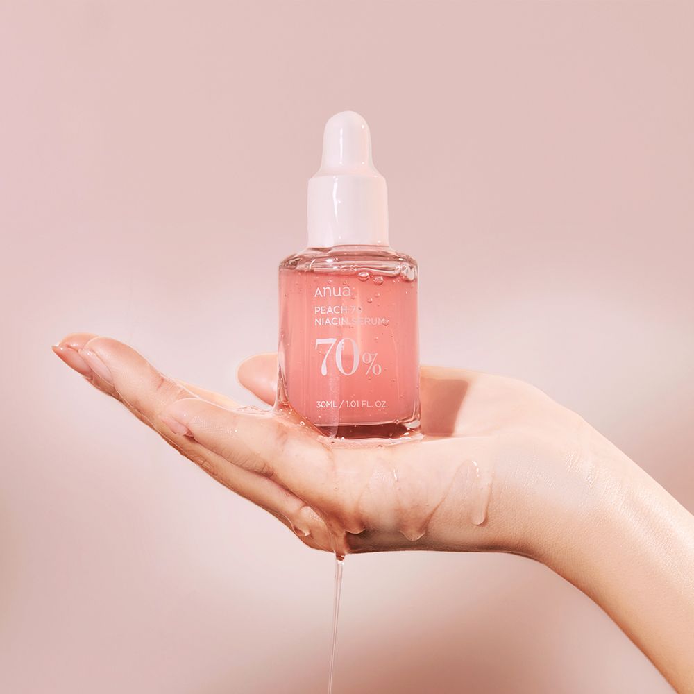 Hand houdt Anua Peach 70 Niacin serumfles vast, serum druppelt.