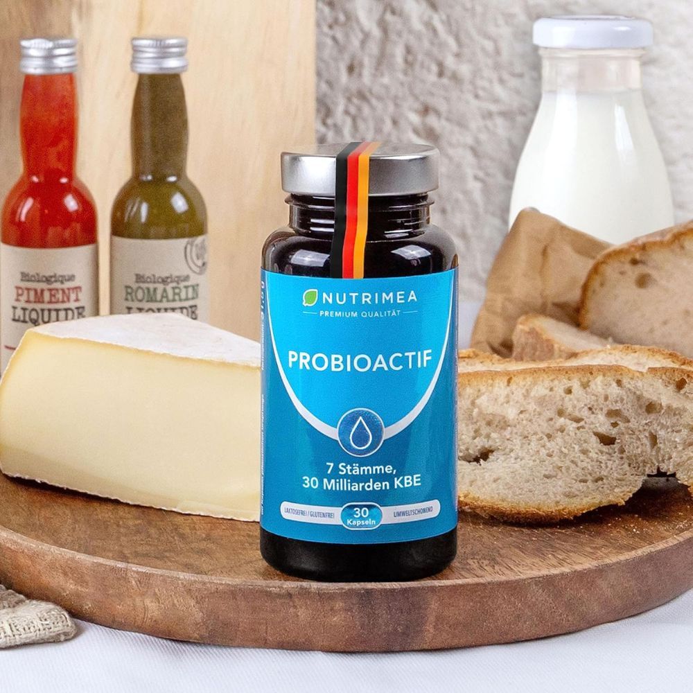 Fles PROBIOACTIF omringd door voedsel: brood, kaas, sauzen, melk. 7 stammen, 30 miljard KVE.