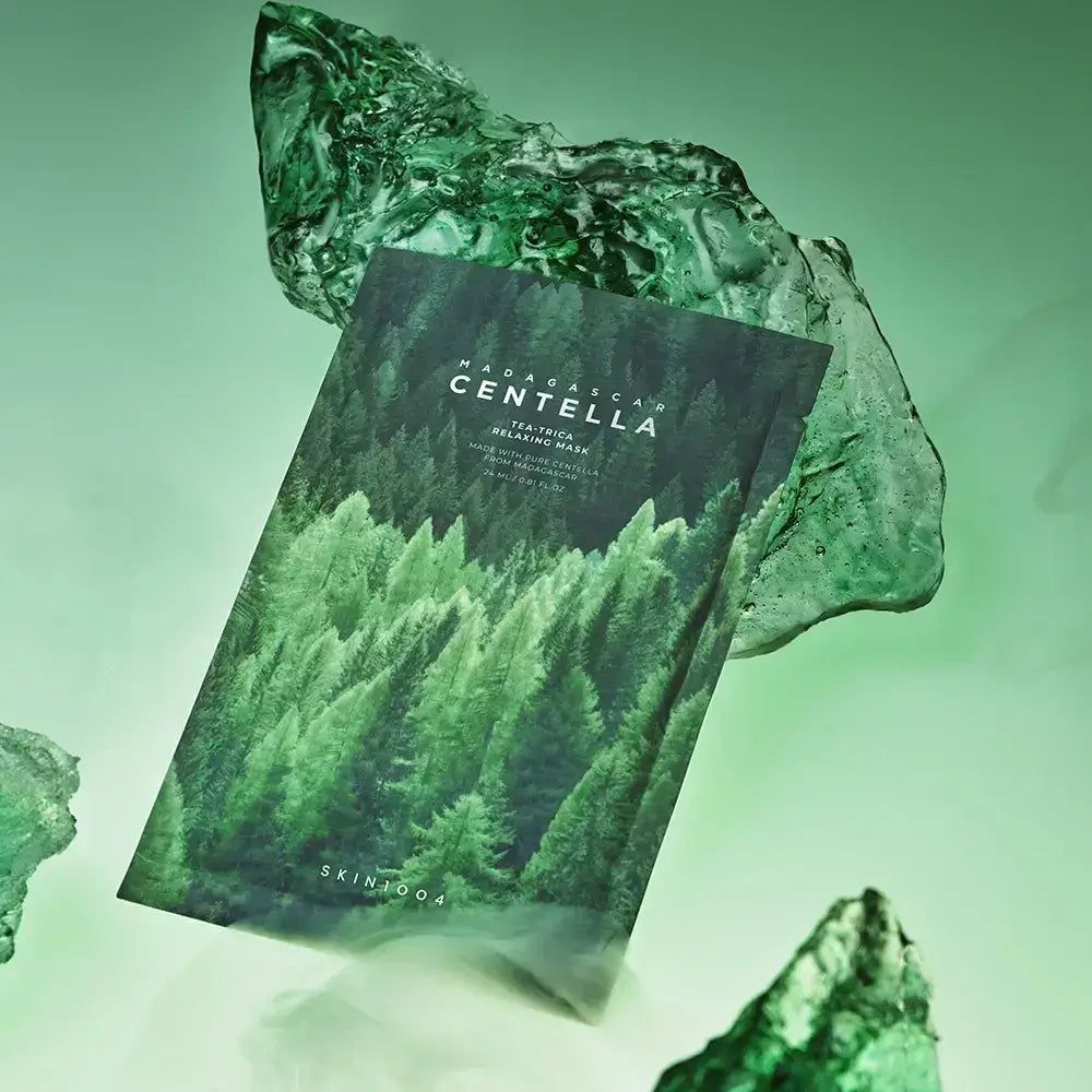 Emballage de masque facial avec motif forêt et inscription MADAGASCAR CENTELLA. Entre des morceaux de verre vert.