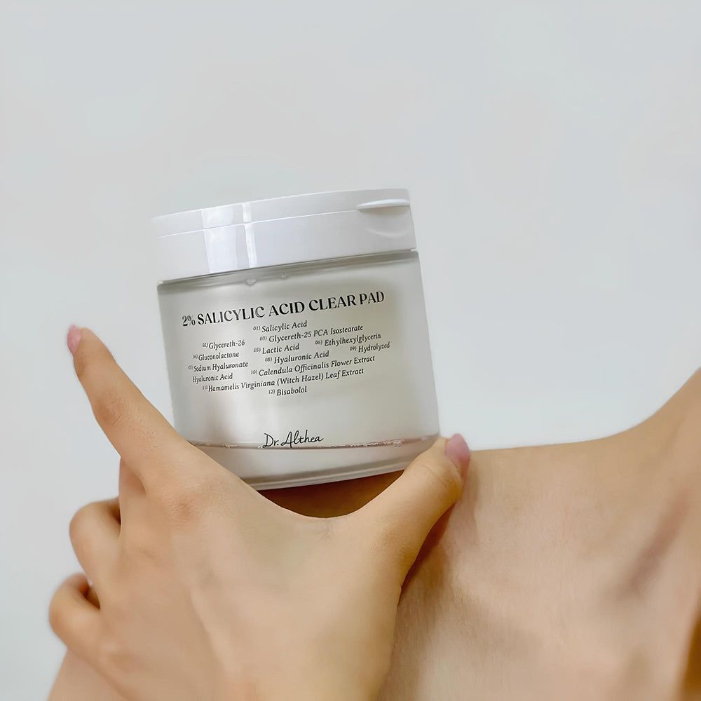 Dr. Althea 2% Salicylic Acid Clear Pad in een glazen pot, vastgehouden door een hand.