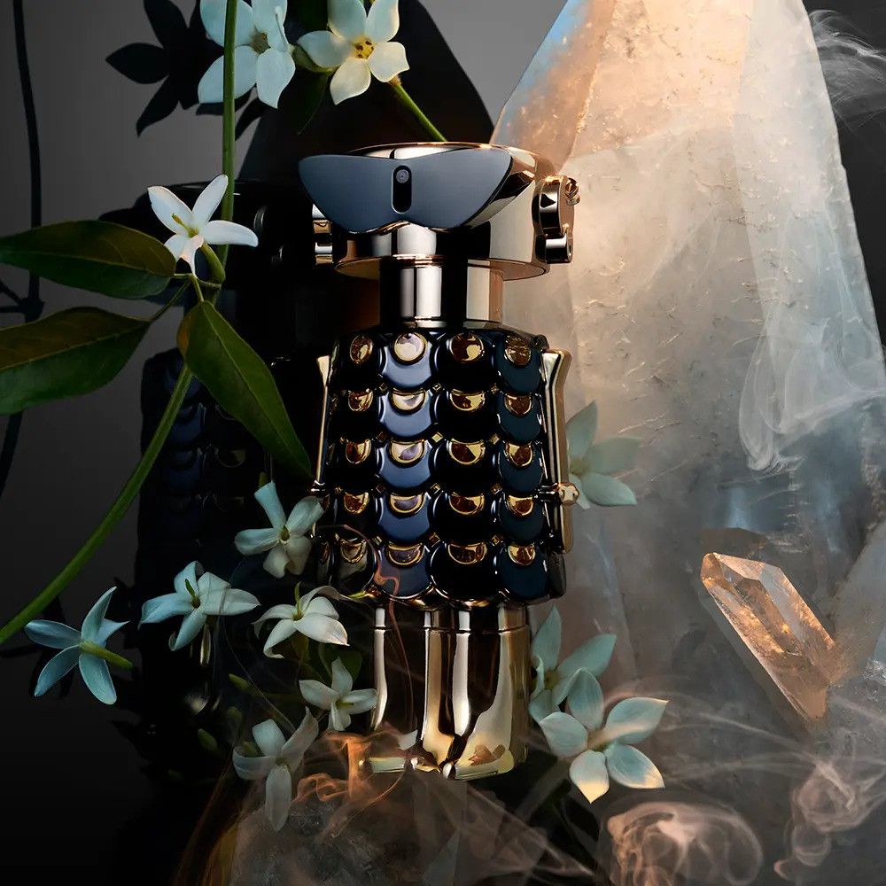 Flacon de parfum noir et or, entouré de fleurs blanches et de cristaux.