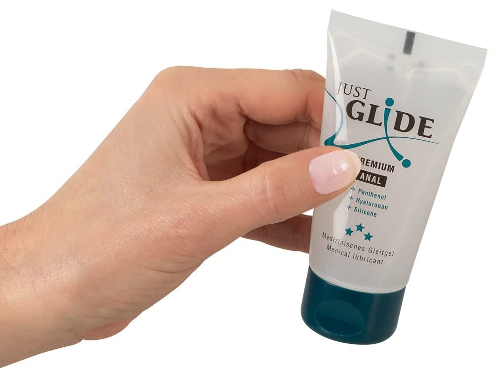 Main tenant un tube de gel lubrifiant Just Glide Premium Anal. Récipient transparent avec bouchon bleu.