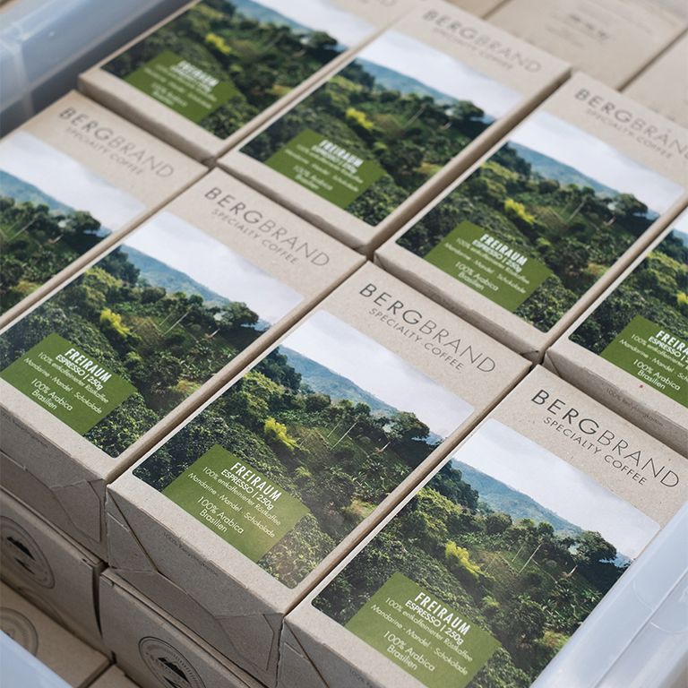 Plusieurs paquets de café dans une boîte. Texte: BERGBRAND, Specialty Coffee, Freiraum Espresso, 100% Arabica, Brésil.