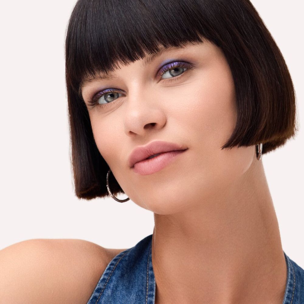 Portrait d'une femme aux cheveux foncés et au maquillage bleu sur les yeux. Elle porte des créoles argentées. Son regard est dirigé vers la caméra.