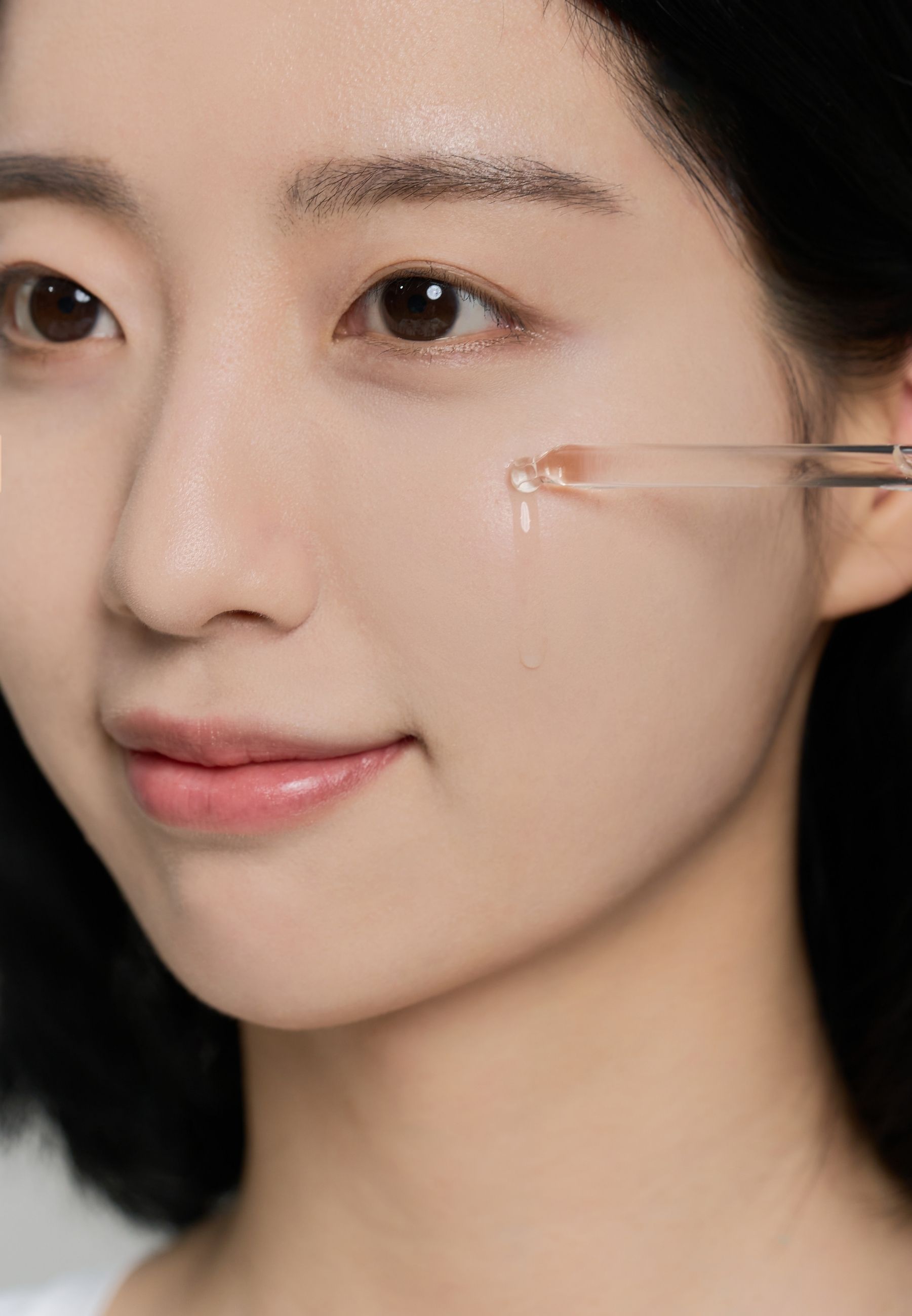 Vrouw die vloeistof op haar huid aanbrengt met een pipet. Close-up van gezicht.