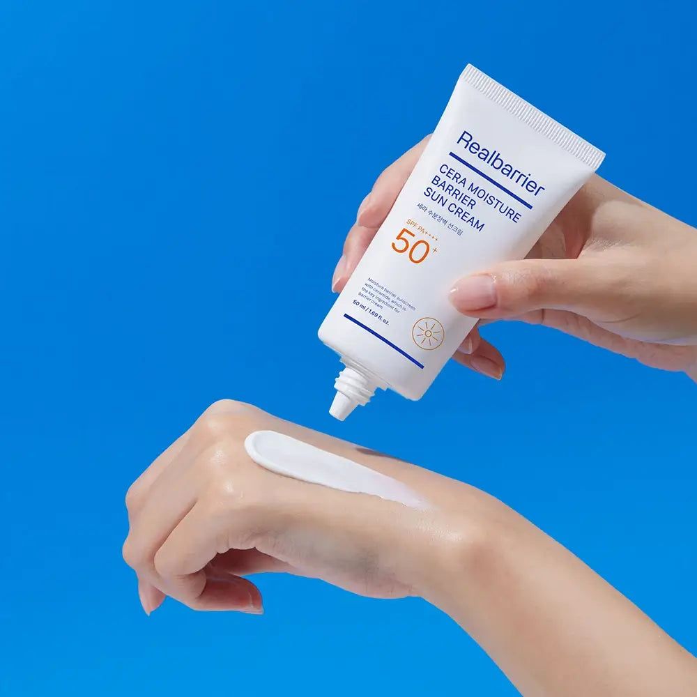 Tube blanche de crème solaire Realbarrier. Crème appliquée sur la main. Inscription: Cera Moisture Barrier Sun Cream SPF 50. Crème claire.