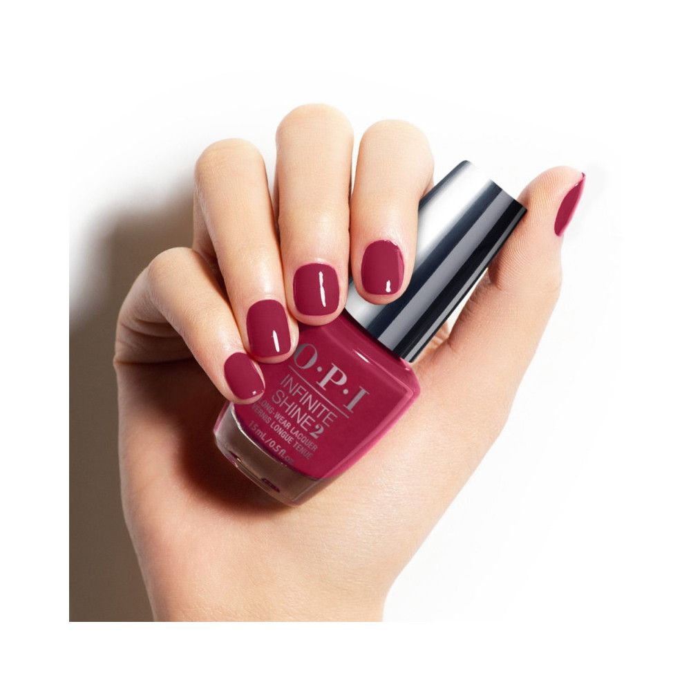 Hand houdt een fles nagellak vast. Dezelfde tint is aangebracht op de vingernagels.