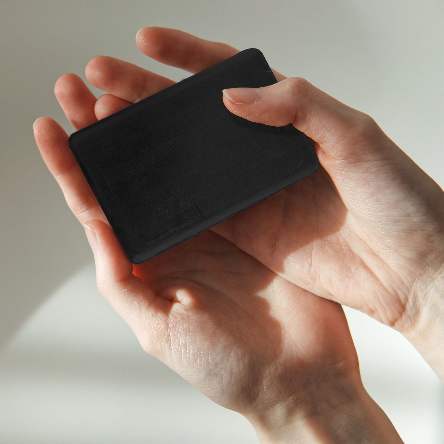 Savon noir rectangulaire tenu dans les mains. Texture légère.
