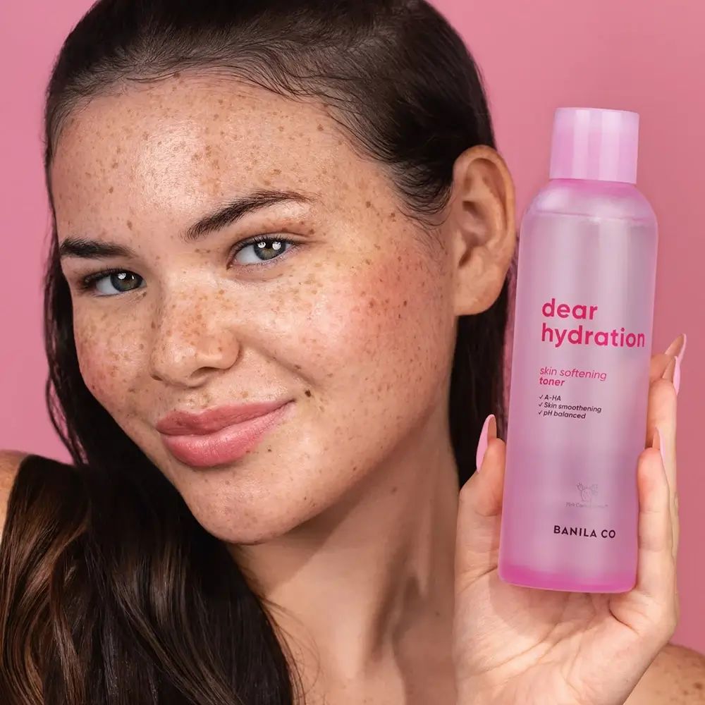 Vrouw houdt een roze fles vast. Opschrift: dear hydration, skin softening toner. Merk: BANILA CO.