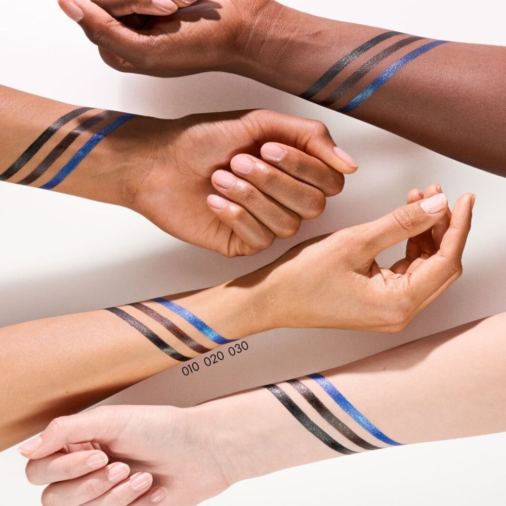 Drie armen met parallelle, glinsterende eyelinerstrepen in blauw, zwart en grijs. Cijfers 010, 020, 030 zijn zichtbaar.