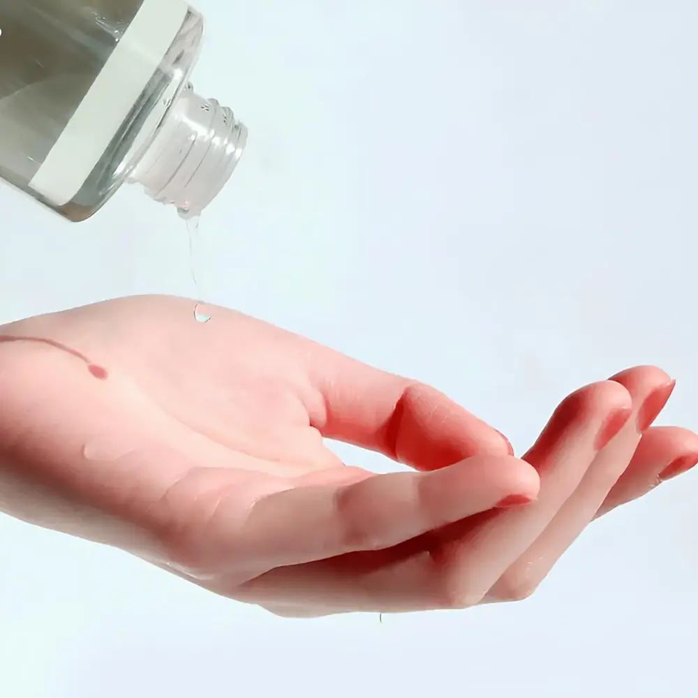 Hand met rode nagellak die vloeistof uit een fles opvangt. Vloeistof druppelt op de handpalm.