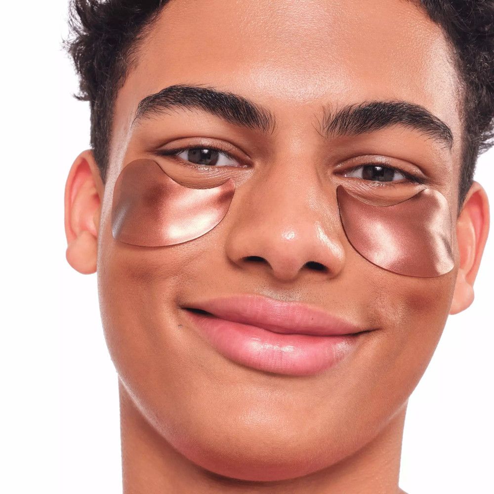 Gros plan d'un homme avec des patchs pour les yeux. Patchs en forme d'yeux, brillants, bruns. L'homme sourit.