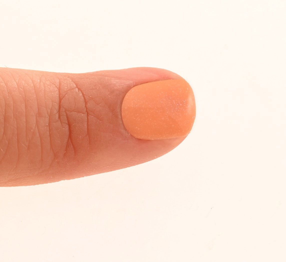Doigt avec ongle verni. L'ongle est recouvert d'un vernis à ongles orange.