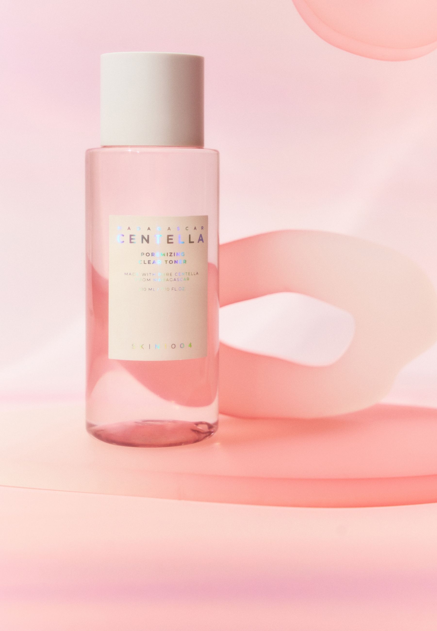 Roze vloeistof in een fles. Op roze sokkel. Decoratieve elementen op de achtergrond.