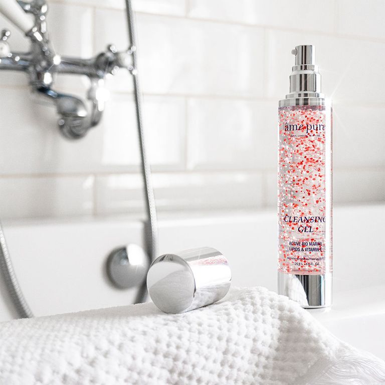 Un flacon de gel nettoyant avec particules rouges est posé sur une serviette dans une salle de bain.