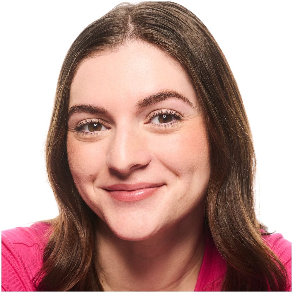 Portrait d'une femme souriante aux cheveux bruns. Elle porte un haut rose. Maquillage naturel.