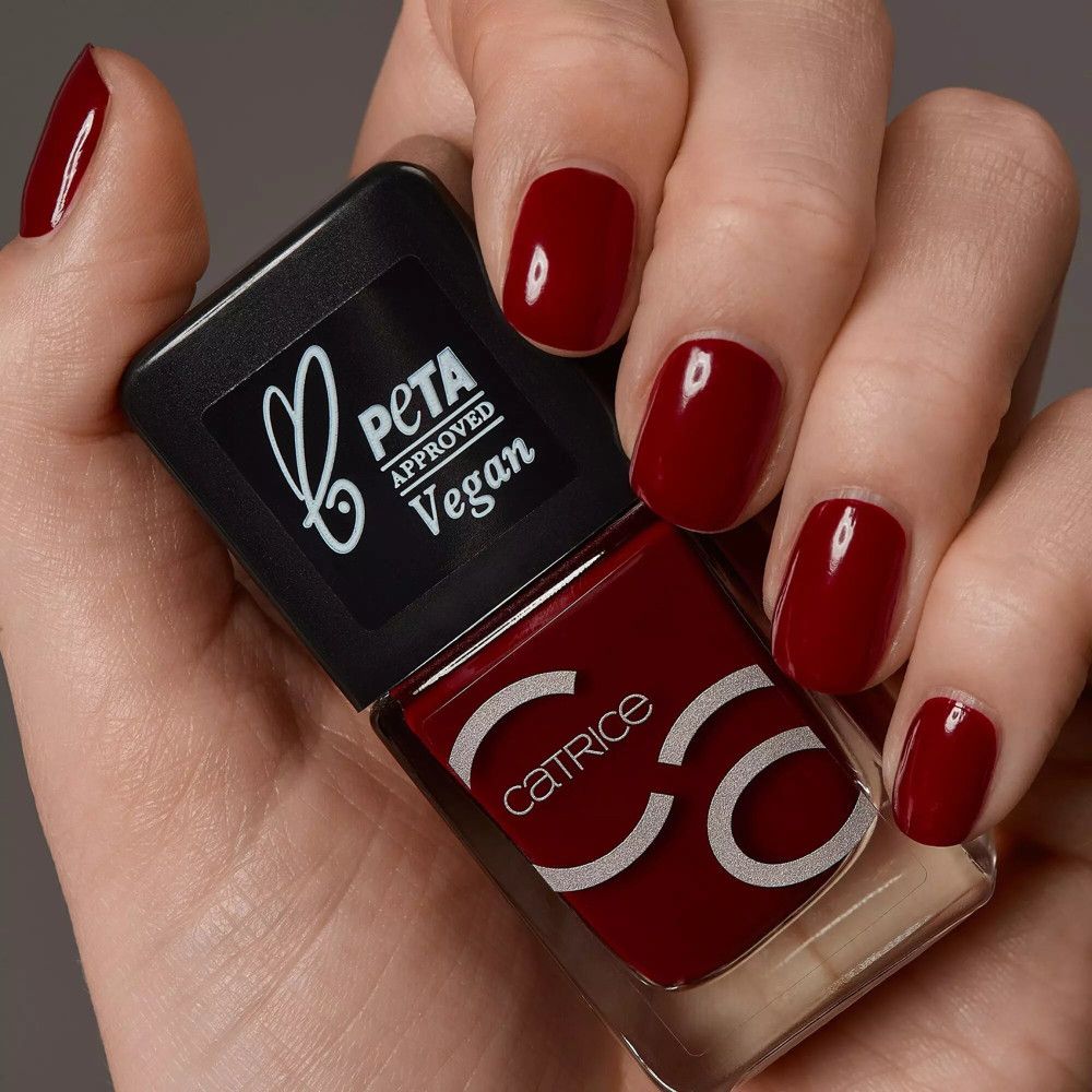 Main avec ongles vernis et flacon de vernis à ongles. Catrice et PETA Vegan sont sur le flacon.