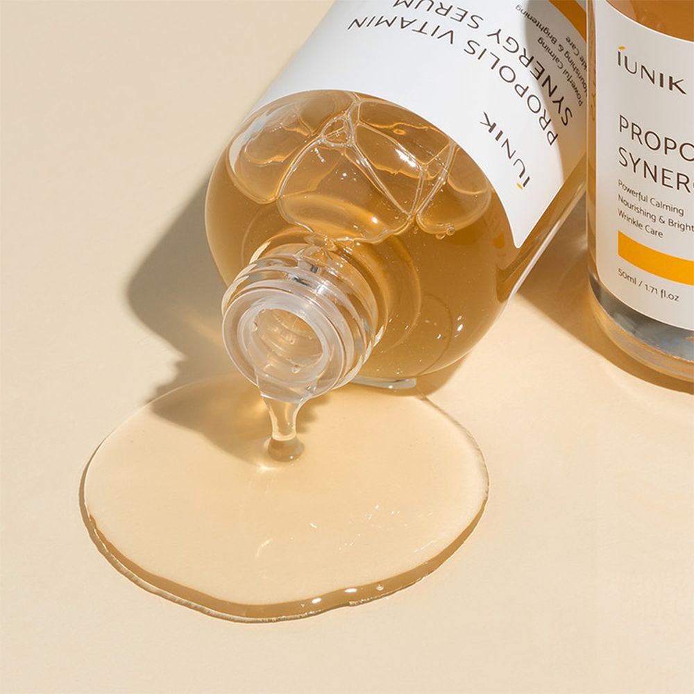 Le Sérum Synergie Propolis Vitamine iUNIK coule d'une bouteille. Le sérum est jaune doré.