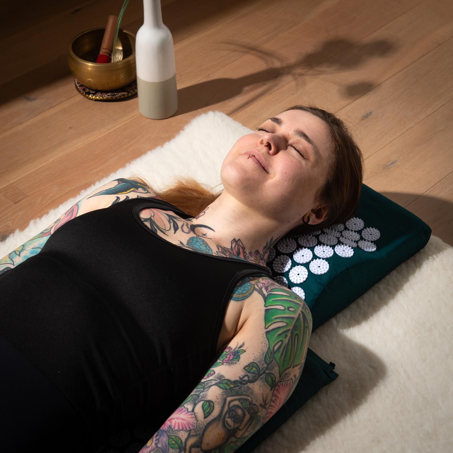 Personne allongée sur un coussin d'acupression. Coussin vert foncé à picots blancs. Personne tatouée.