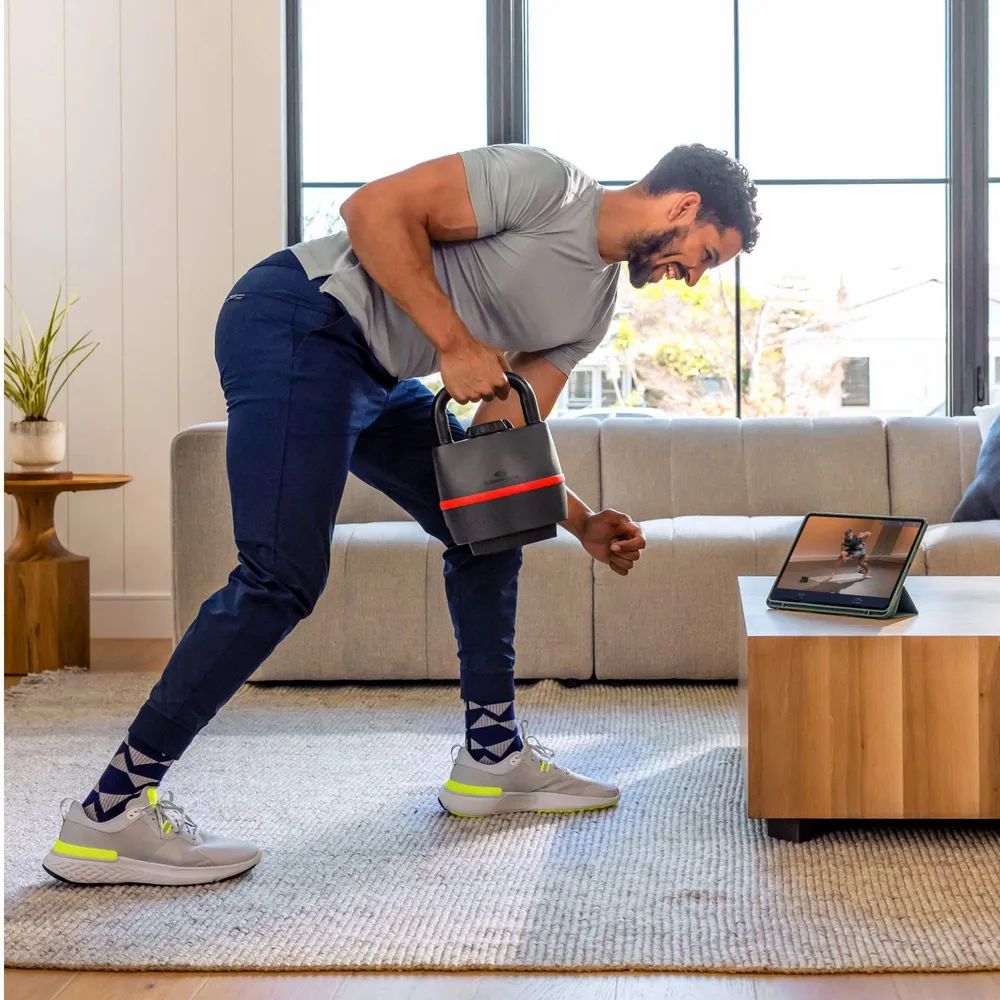 Homme avec kettlebell. Haltère russe noire avec bande rouge. Logo Bowflex visible.