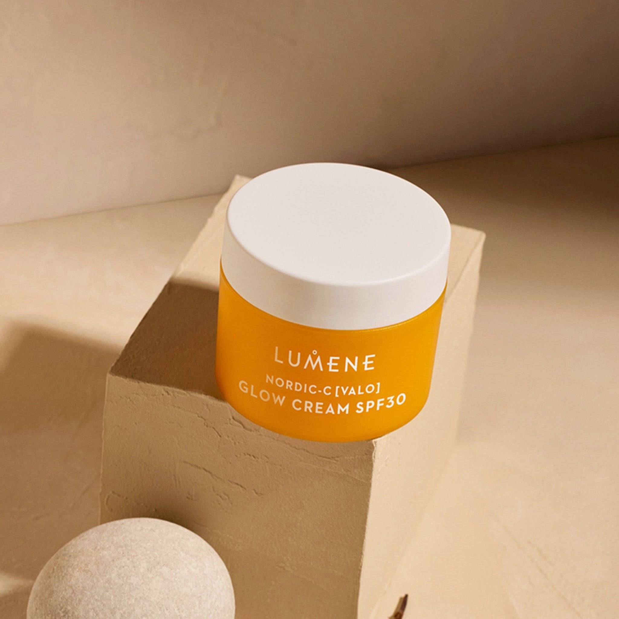 Pot de crème jaune avec couvercle blanc sur socle. Inscription : LUMENE, NORDIC-C [VALO] GLOW CREAM SPF30.