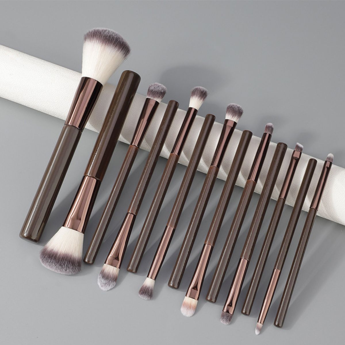 Un ensemble de 12 pinceaux de maquillage foncés avec des accents or rose et des poils doux.
