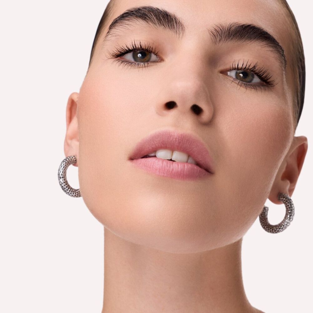 Gros plan d'un visage avec créoles argentées. La femme a des sourcils foncés et des lèvres.