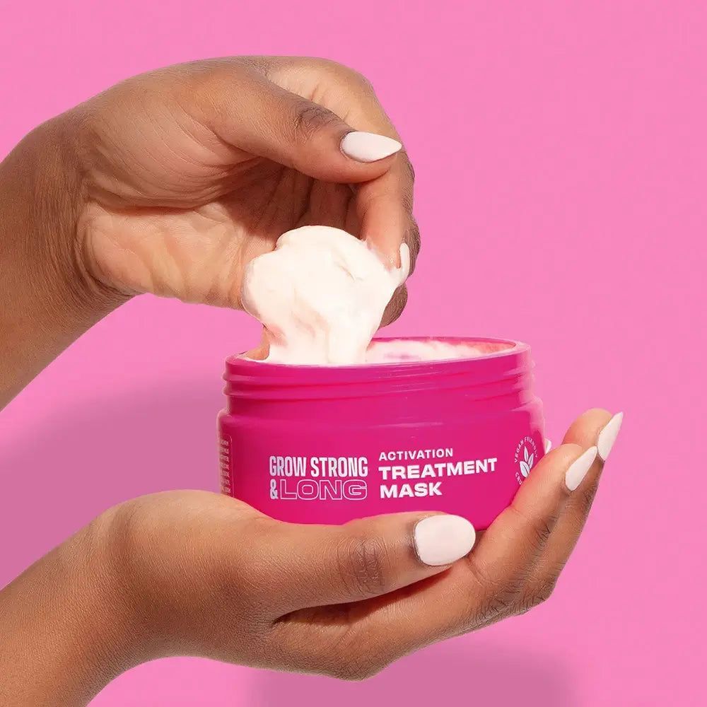 Handen halen een romig masker uit een roze pot 'Grow Strong & Long'.