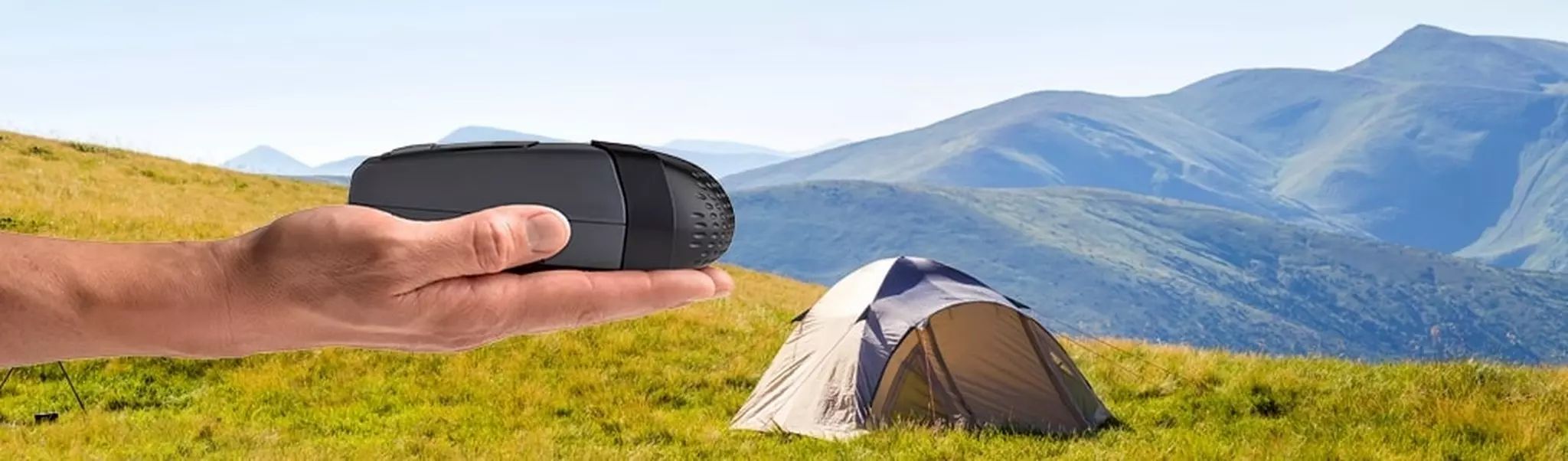 Appareil CPAP de voyage gris compact dans une main, devant un paysage de montagne et une tente.