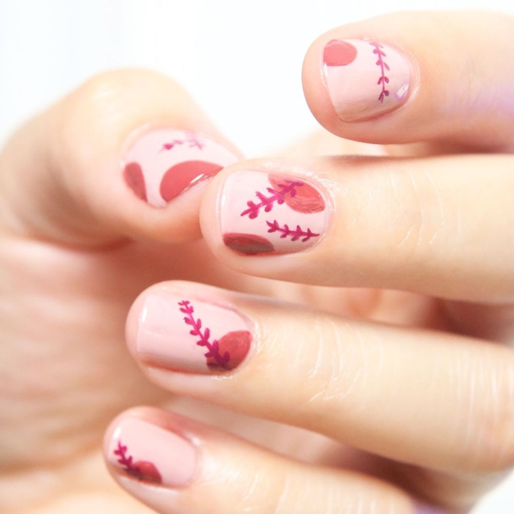 Close-up van een hand met roze gelakte nagels. Rode blad- en stippenpatronen op de nagels.