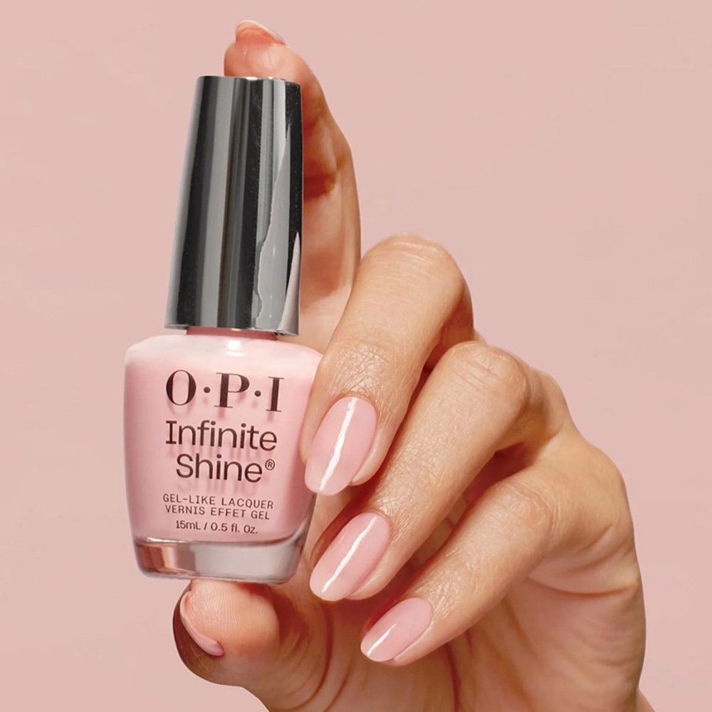 Flacon de vernis à ongles rose. Logo OPI Infinite Shine. Main tenant le flacon avec des ongles vernis.