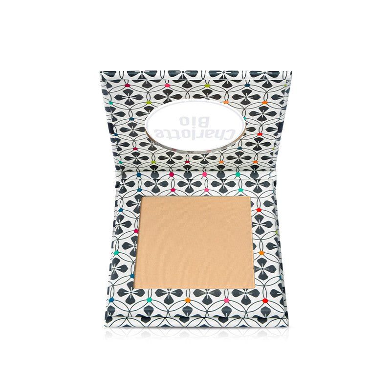 Poudre compacte dans un emballage ouvert. L'emballage est décoré d'un motif. La poudre est de couleur beige clair.