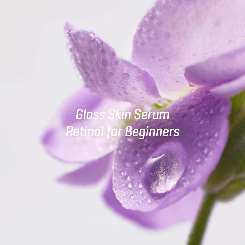 Gros plan d'une fleur violette avec des gouttes d'eau. Texte : Glass Skin Serum Retinol for Beginners.