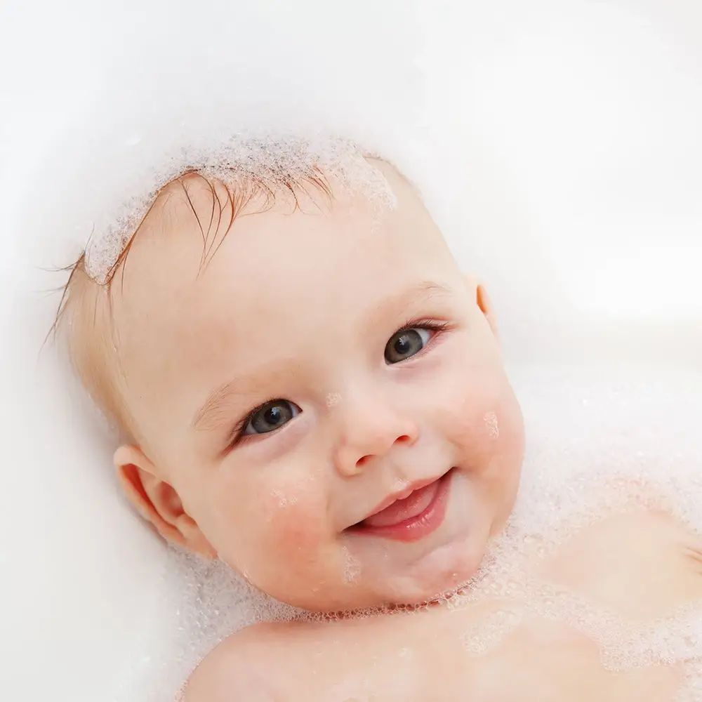 Gros plan d'un bébé dans un bain. Le bébé sourit et est couvert de mousse.