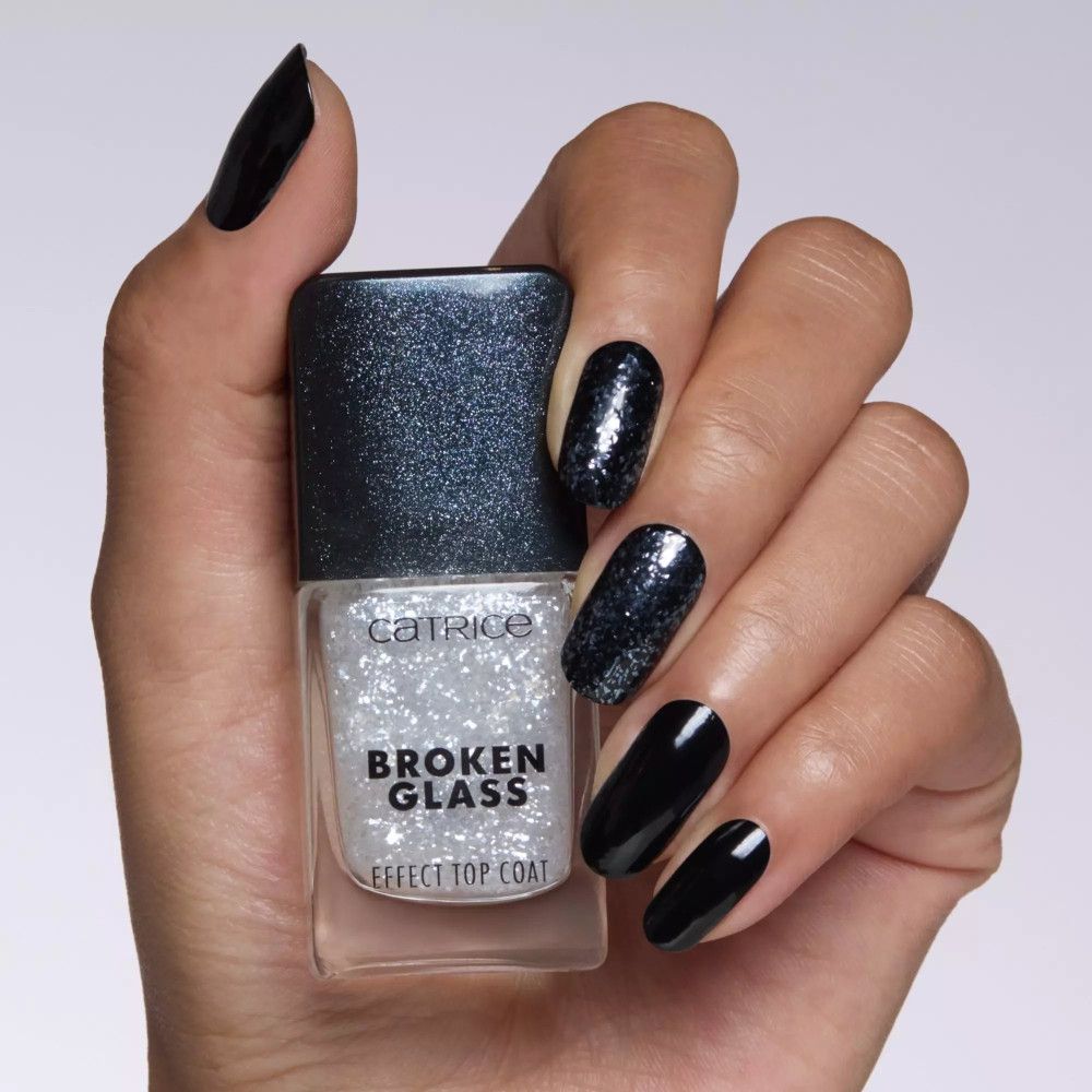 Main tenant le top coat Catrice effet verre brisé. Ongles vernis noirs, un avec paillettes.