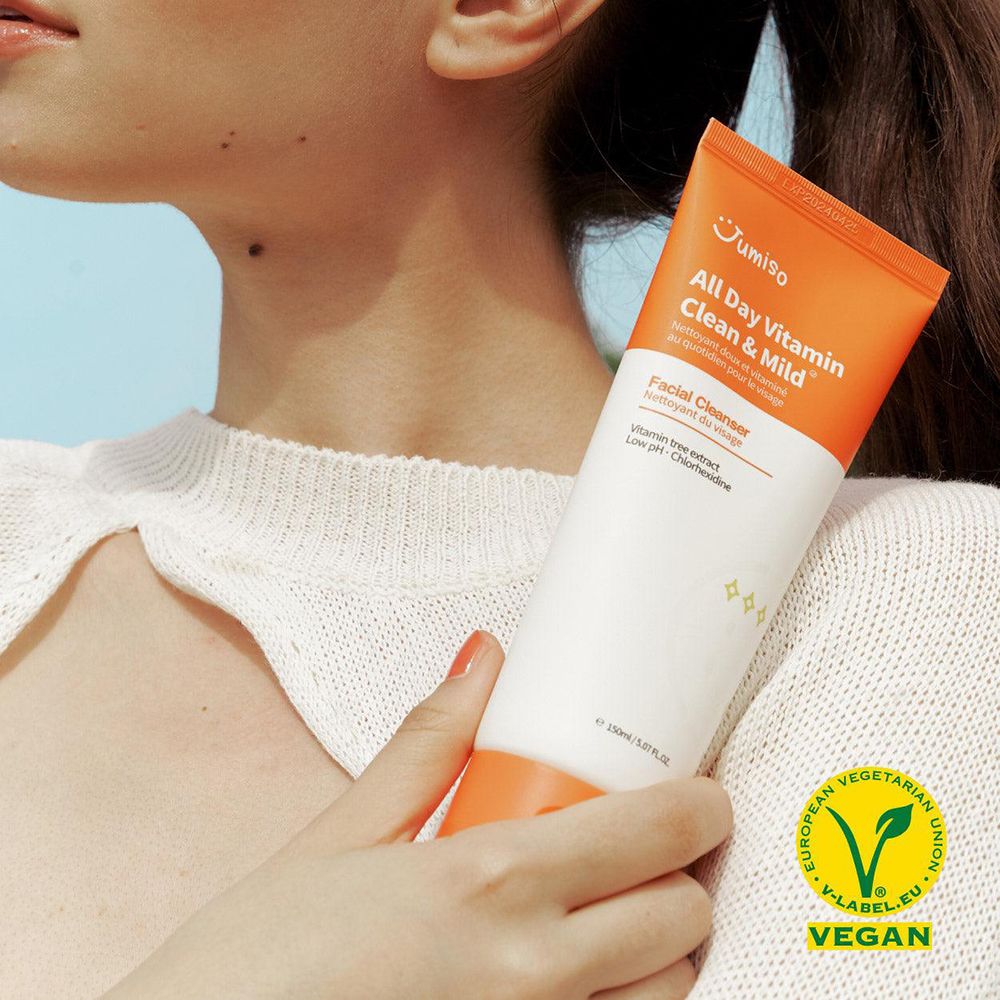 Persoon houdt een tube vast. Opschrift: All Day Vitamin Clean & Mild. Vegan-zegel. Gezichtsreiniger.