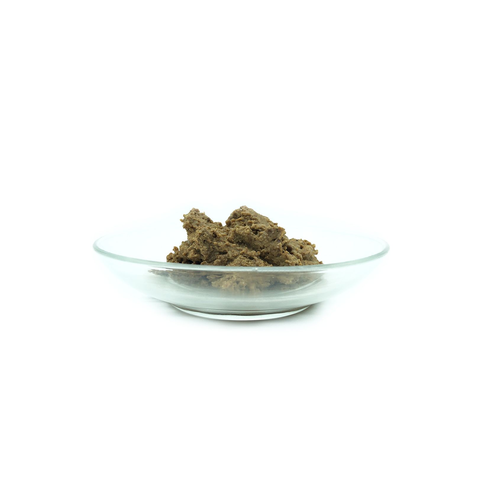 Aliments pour chiens dans un bol en verre. La nourriture est brune et de forme irrégulière. Le bol est rond et transparent.