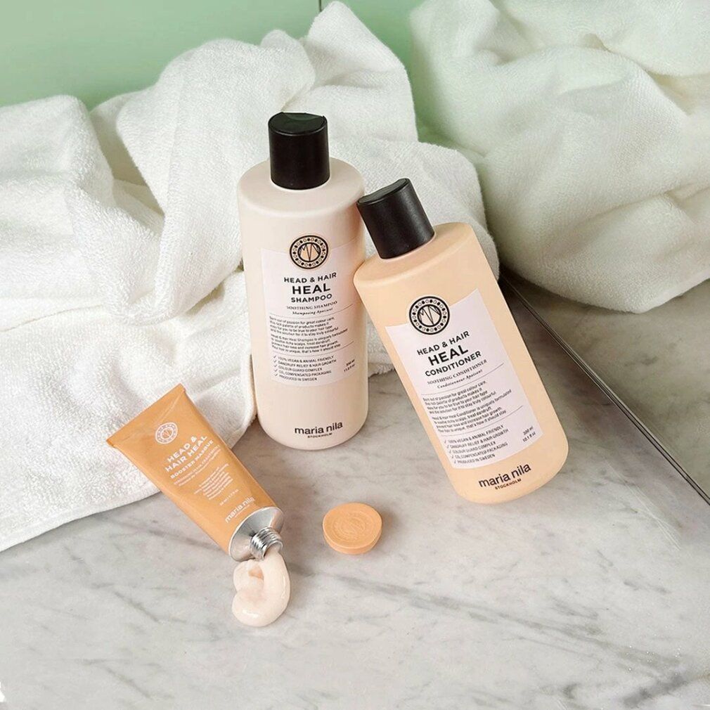 Maria Nila producten: shampoo, conditioner en crème. Beige flessen en tube. Op marmeren oppervlak met handdoeken. Productnamen zichtbaar.
