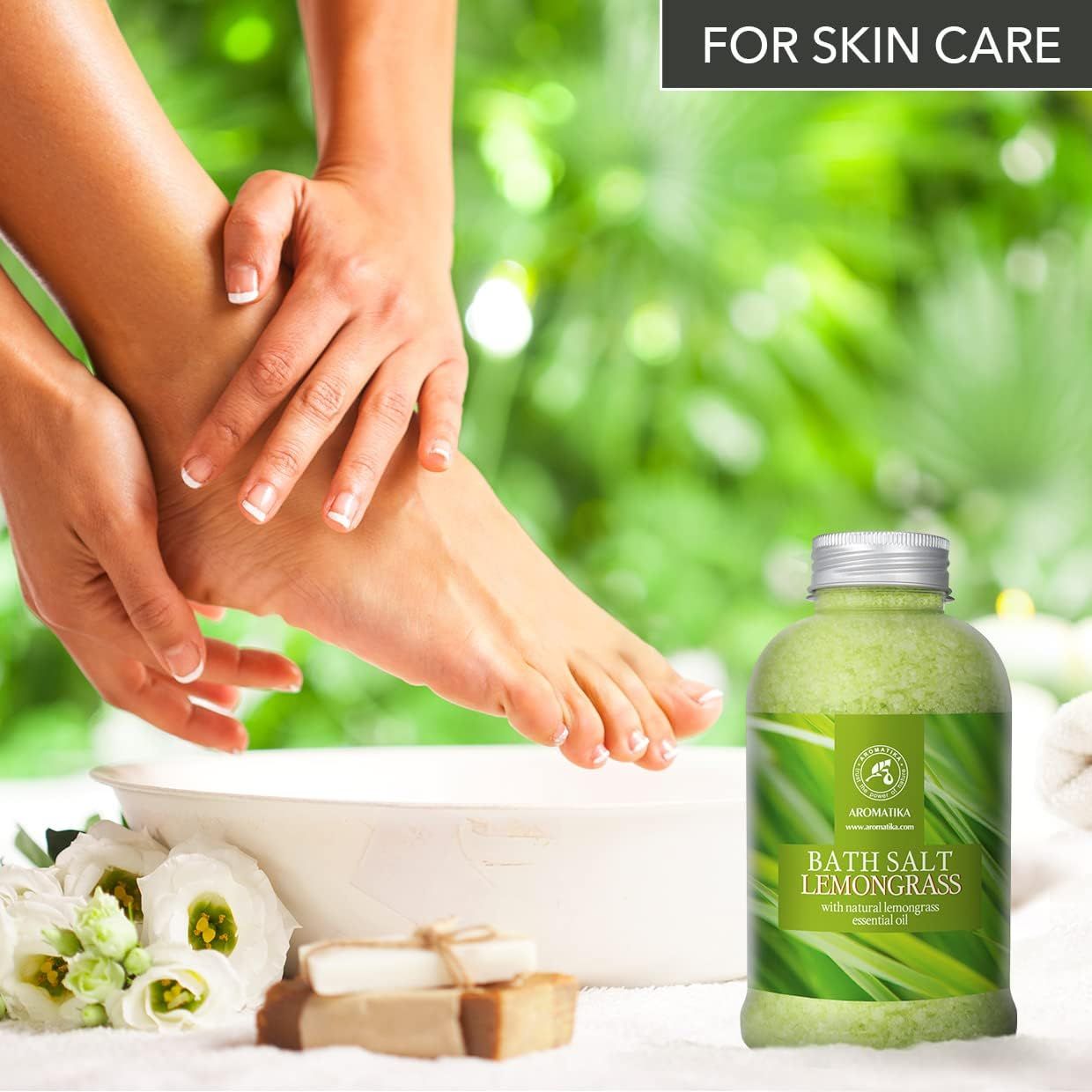 Mains massant les pieds au-dessus d'un bol. Morceaux de savon et AROMATIKA Sel de bain Lemongrass à côté.